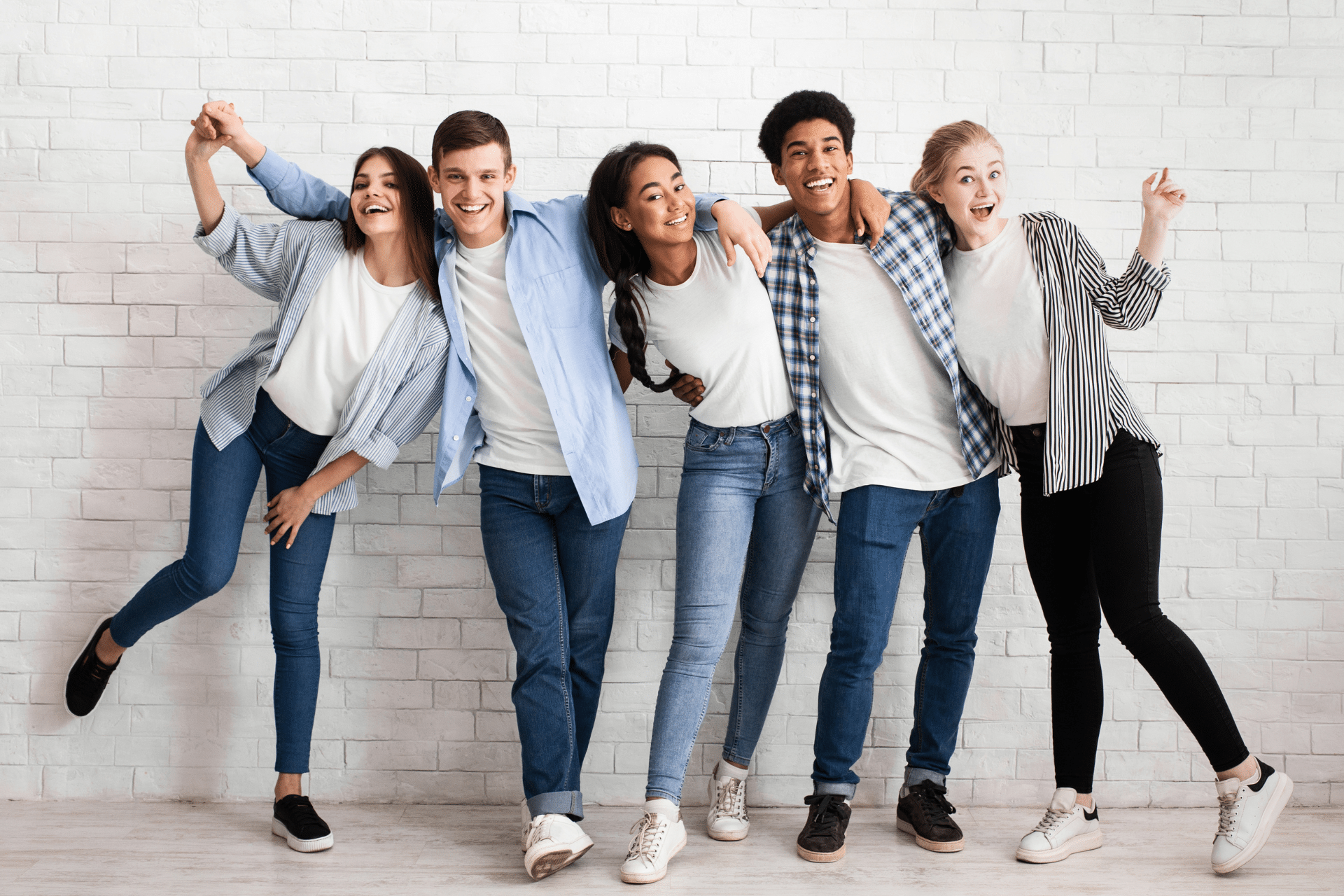 Group of smiling college-age friends standing together against a white brick wall