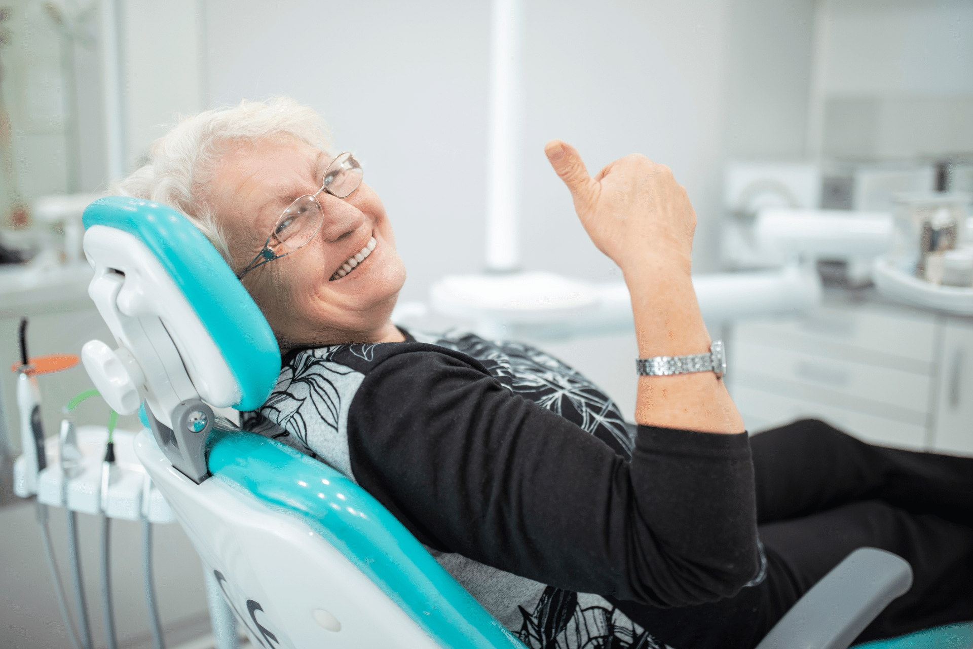 Older adult smiling and giving a thumbs-up while seated in a dental chair