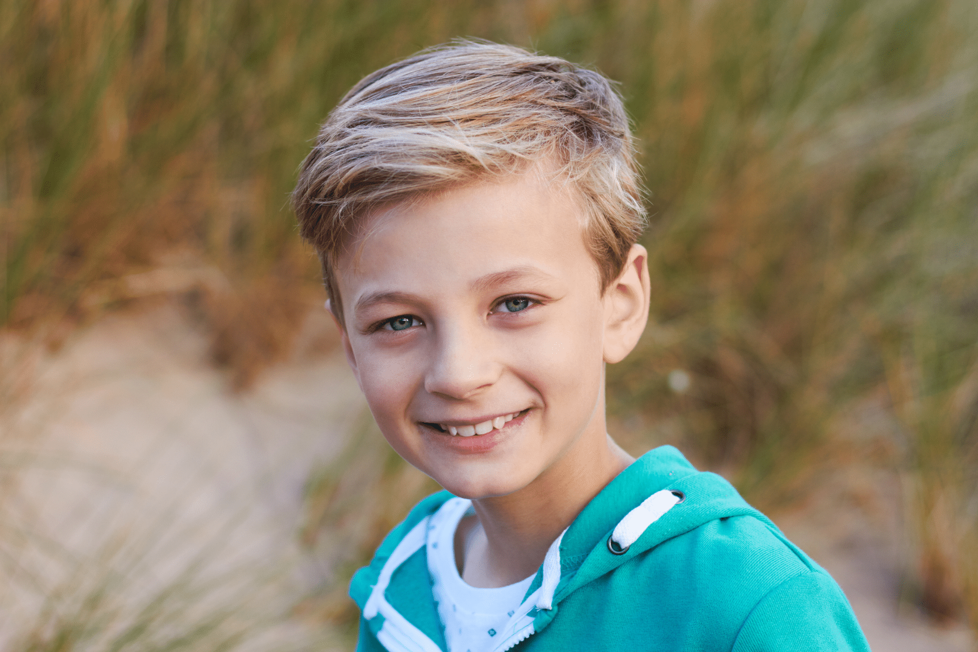 Smiling young boy wearing a teal hoodie outdoors.